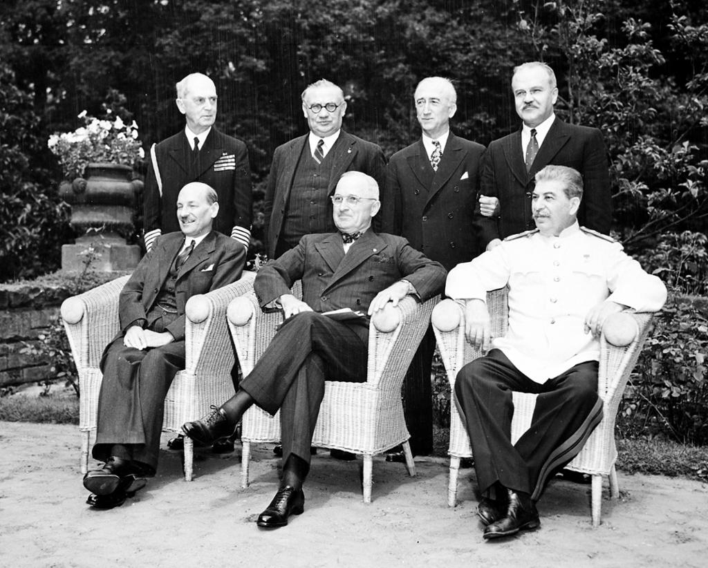 Et gruppebilde med Clement Attlee, Harry Truman, Josef Stalin med flere på Potsdamkonferansen i juli 1945. De tre statslederne sitter i kurvstoler,  de andre mennene står bak dem. De fleste i mørke dresser, Stalin har uniform med hvit jakke. Foto. 