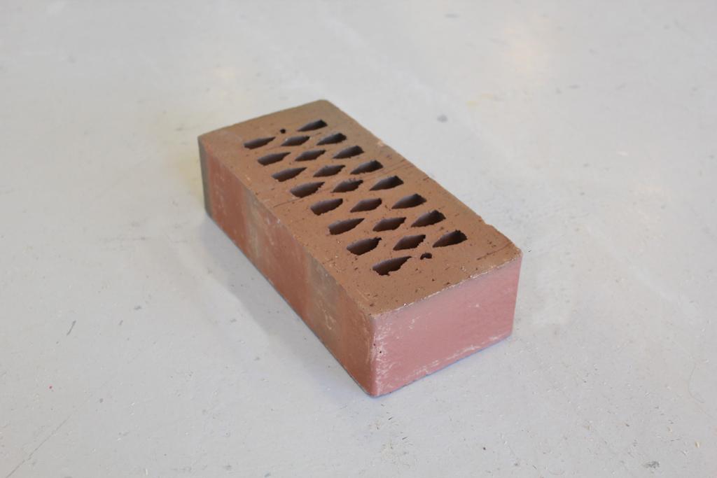 Rødlig prismeformet murstein med prosjektilformede hull. Foto.