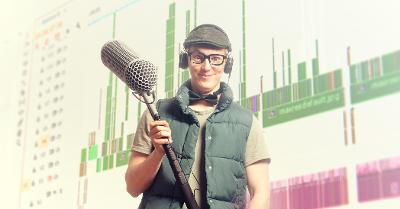 Gutt med briller, hodetelefon, sixpence og boblevest holder en mikrofonbom. Foto.