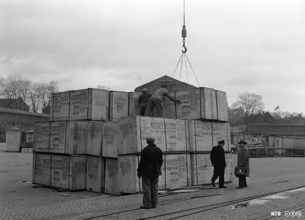 Store kasser med teksten "MASSEY-HARRIS, BETTER FARM EQUIPMENT", losses ved havn i Oslo. Dette var landbruksmaskiner Norge fikk gjennom Marshallhjelpen i 1950. Foto. 
