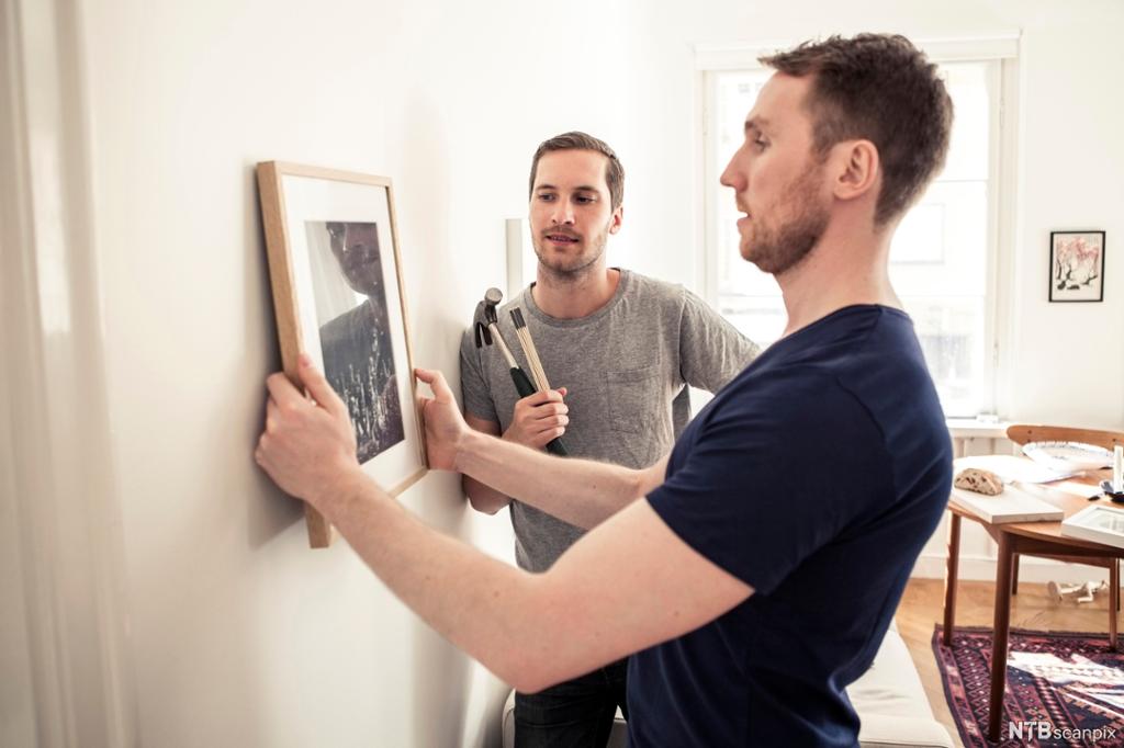 To menn henger opp et bilde på veggen. Foto.
