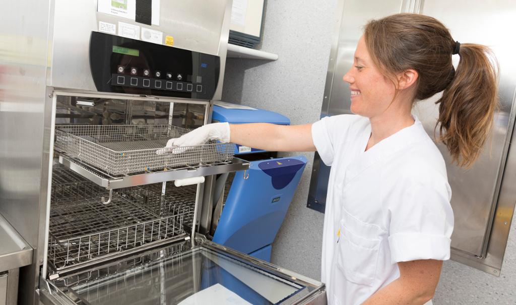 Sykepleier legger brukt utstyr i instrumentvaskemaskin på skyllerommet. Foto.