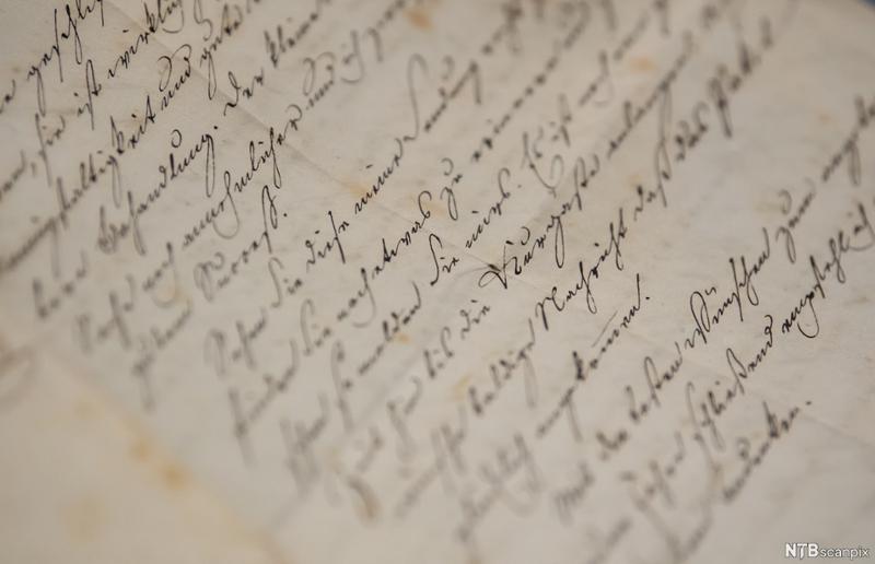 Linjer fra et brev, skrevet med pen, skråstilt løkkeskrift, såkalt gotisk håndskrift. Foto.