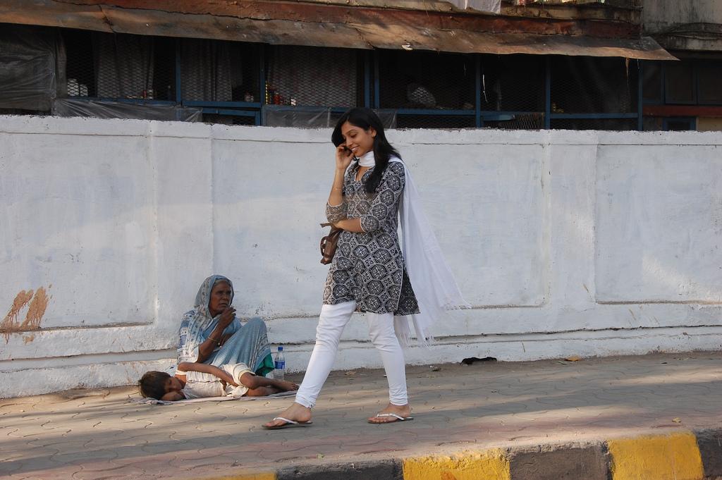 Woman talking on the phone while walking past a homeless woman. Photo.