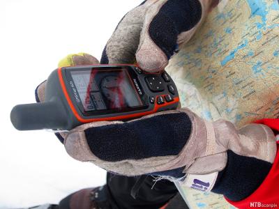 Menneske med kart rund halsen holder en GPS med hanskekledde hender. Foto. 