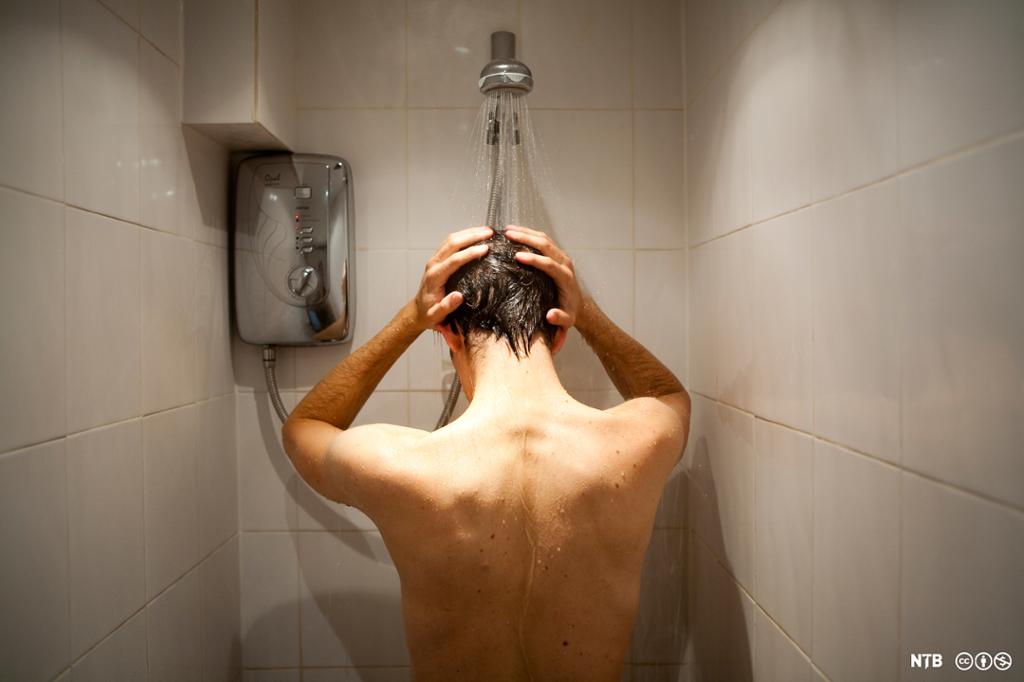 Mann vaskar håret i dusj. Foto.