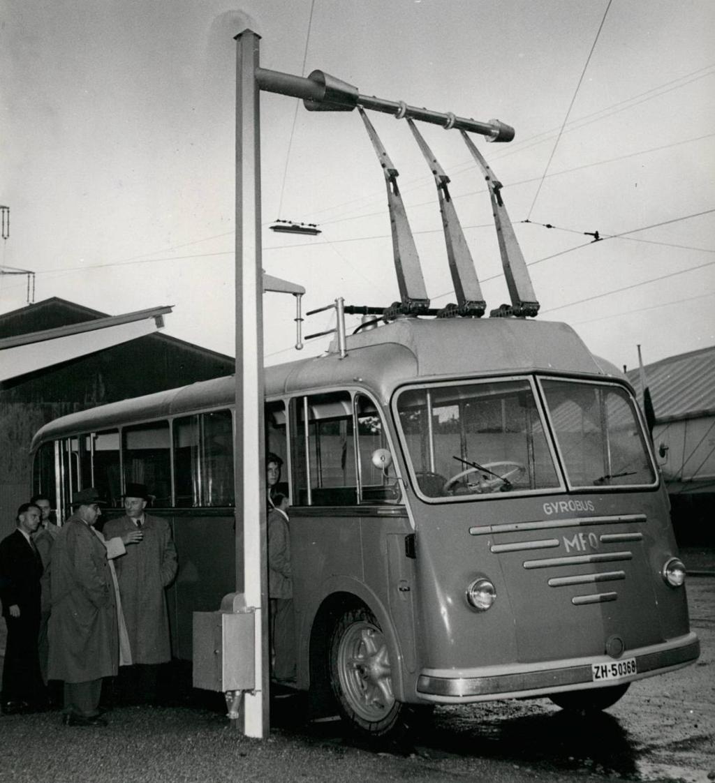 Svartkvittbilete frå 1950-talet av menn i frakk ved ein elektrisk buss. Foto.