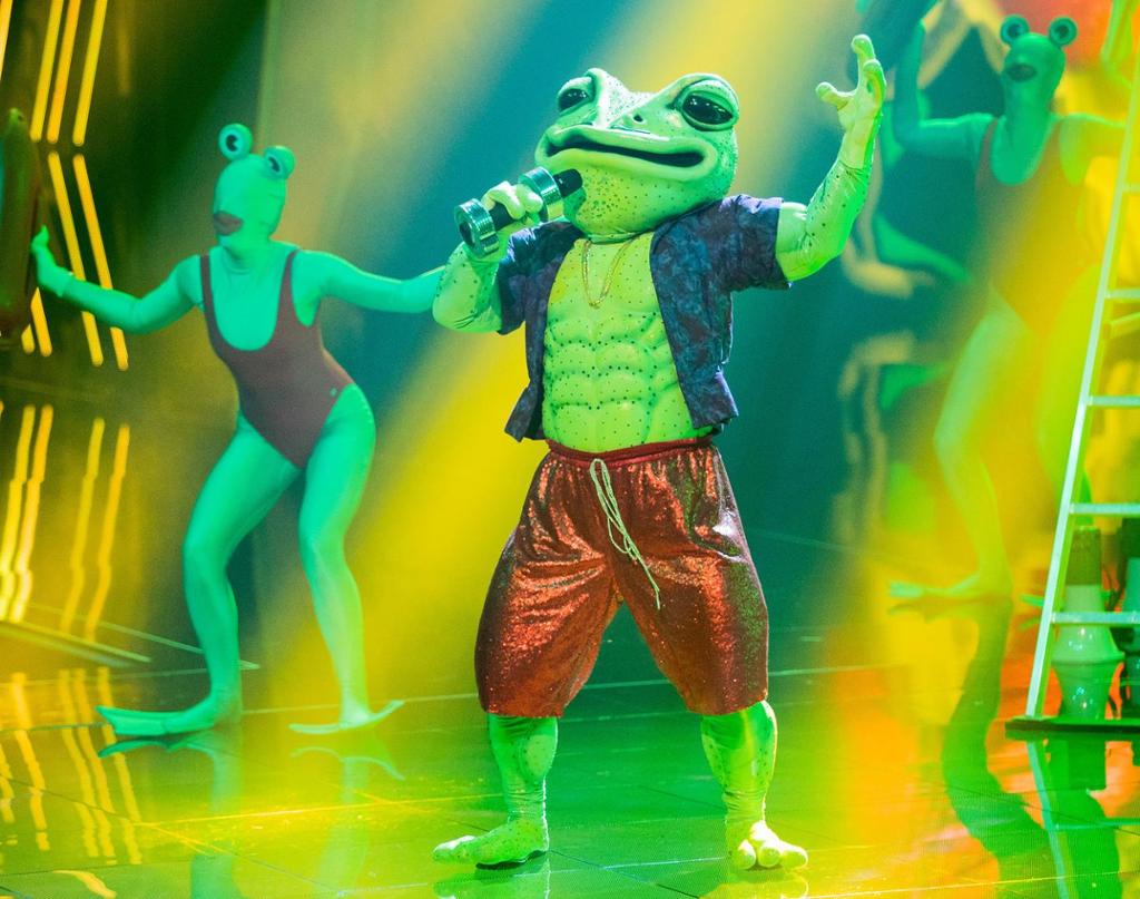 Ein person kledd ut som frosk syng på scena i TV-programmet 𝘔𝘢𝘴𝘬𝘰𝘳𝘢𝘮𝘢. Foto.