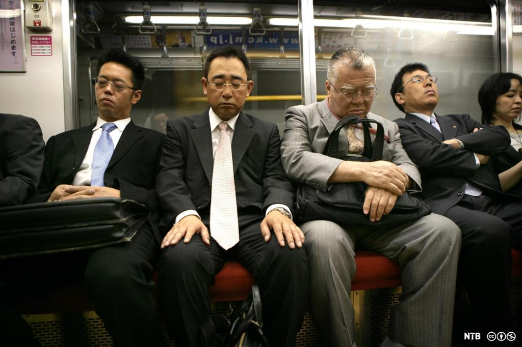 Menn med dress og slips som søv mens dei køyrer T-bane i Tokyo. Foto. 