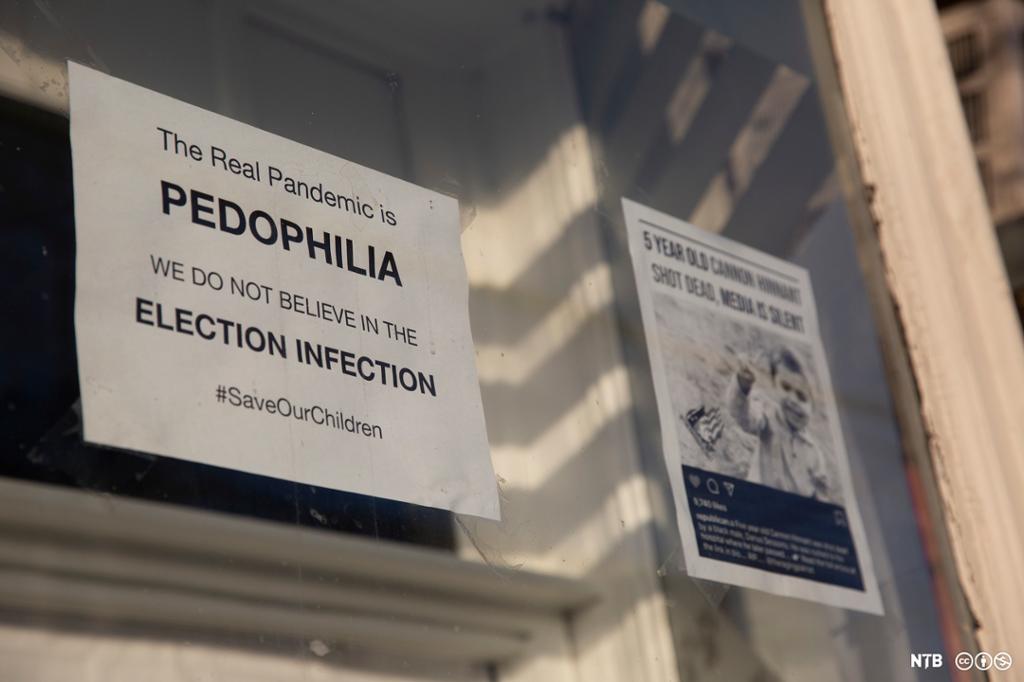 To plakater er hengt opp på et vindu. Den ene advarer om at den ekte pandemien er pedofili, med emneknaggen save our children, og den andre viser et bilde av en liten gutt, som plakaten hevder ble skutt og drept. Foto.