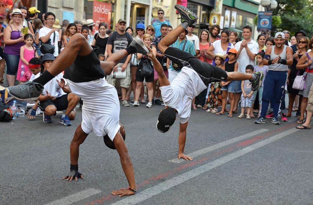 To unge menn står på hender og gjør akrobatisk gatedans. Rundt dem har det samlet seg mange tilskuere. Foto.