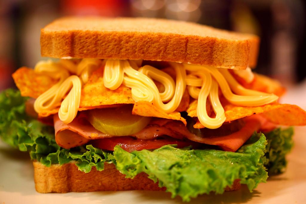 Photo: Closed sandwich with lettuce, tomato, ham, nachos and mayo.