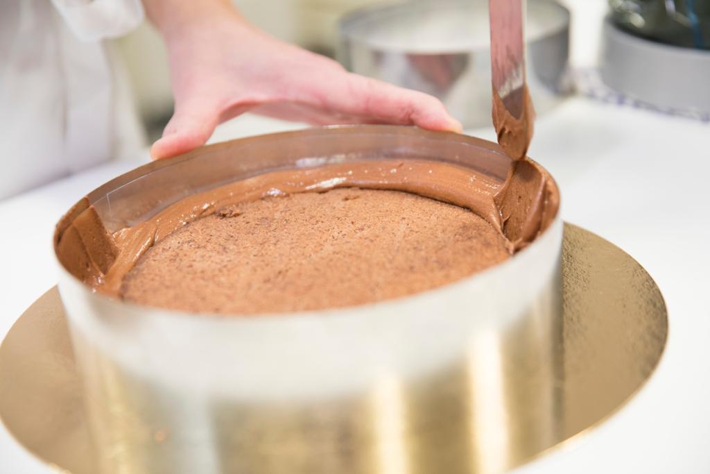 Ein nøttebotn i ei kakeform har fått sjokolademousse sprøytt rundt heile kaka. Ein palett blir brukt til å dra opp moussen langs kanten på heile ringen. Foto.
