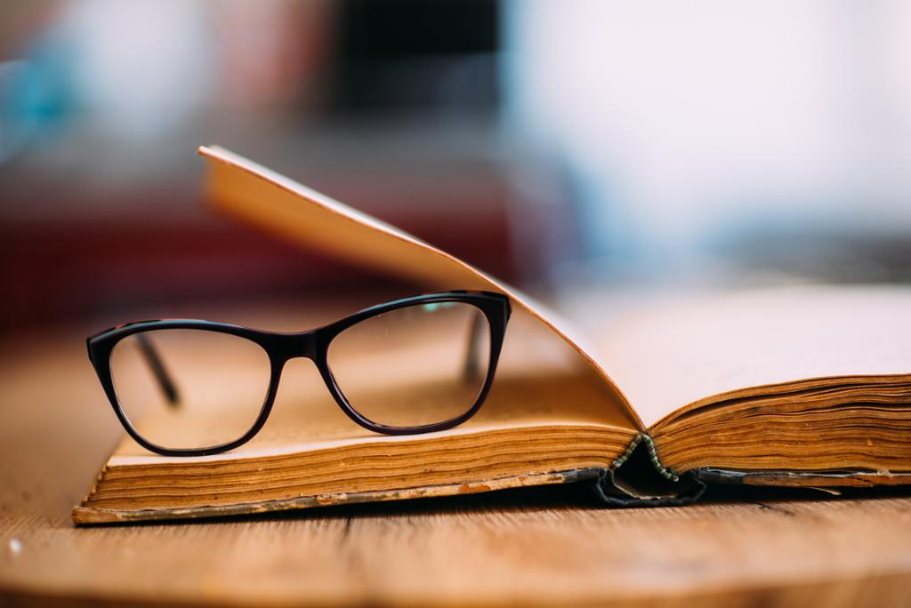 A pair of glasses lying on an old book. Photo. 