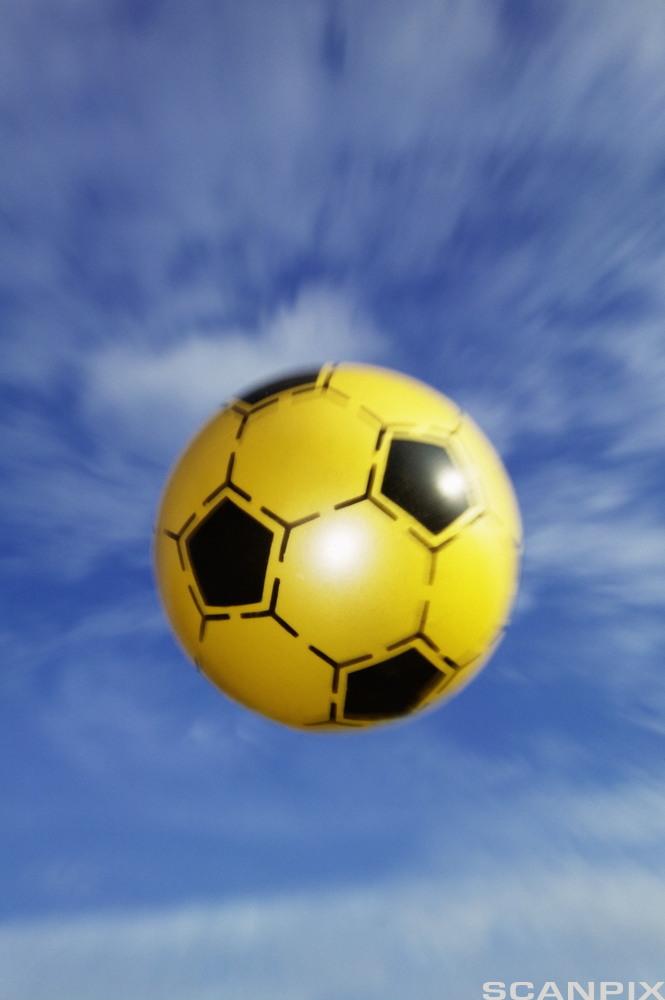 Gul fotball med blå himmel som bakgrunn. Foto.