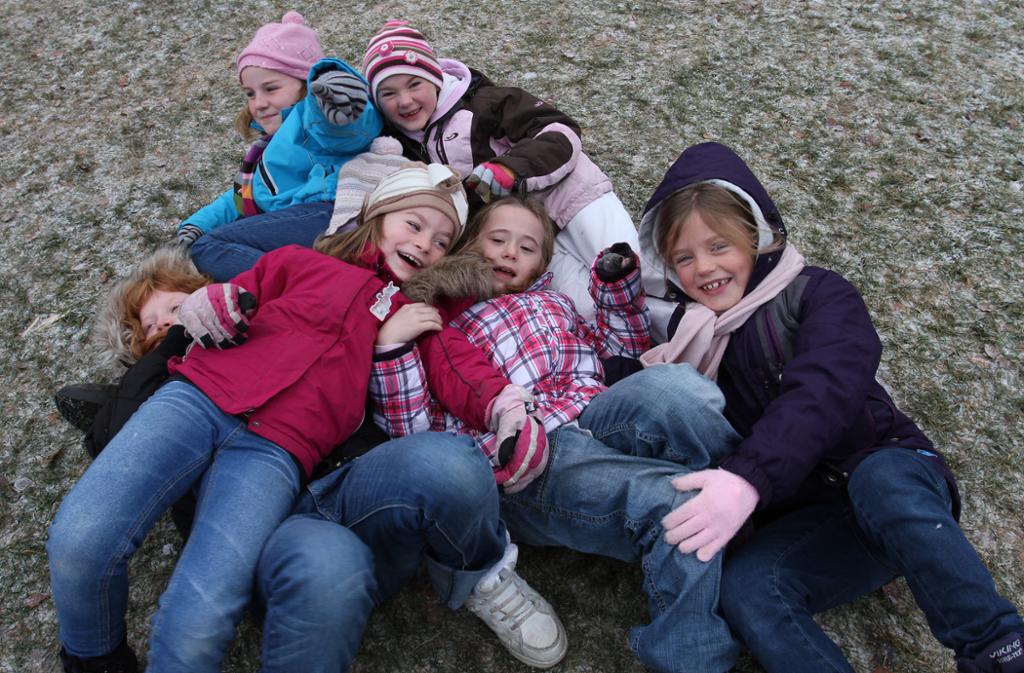Seks barn ligger i en haug på bakken og ler. Foto.