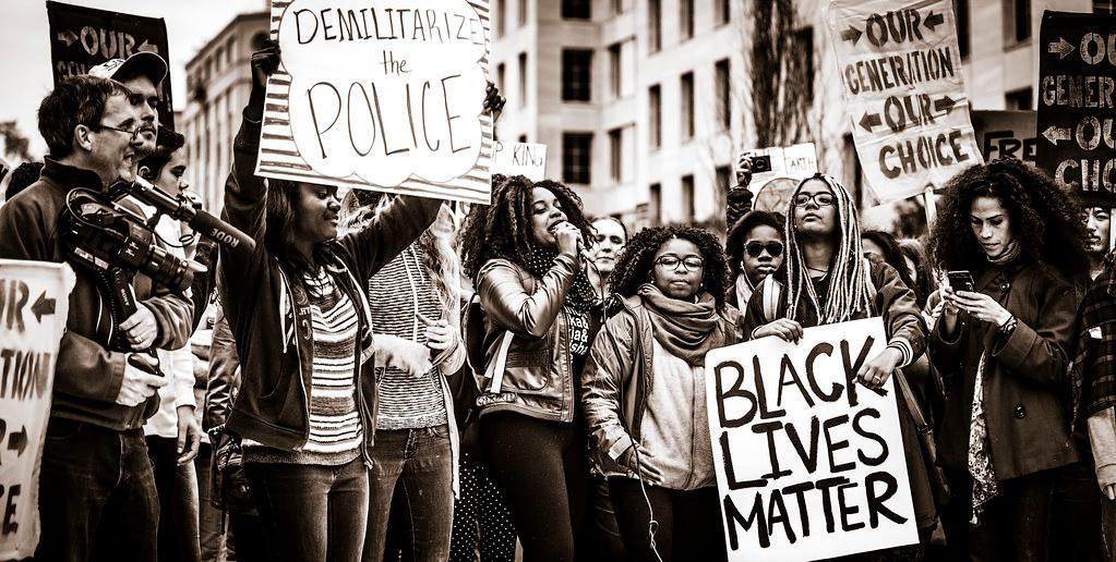 Black and white photo: A group of people demonstrating, holding BlackLivesMatter signs. 