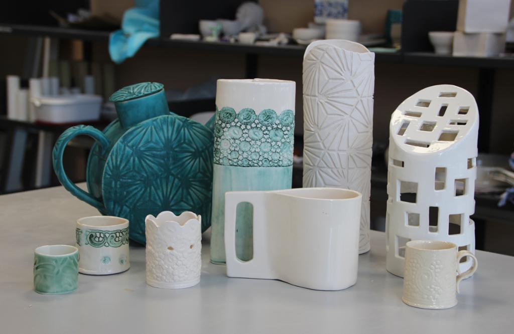 Ulike keramiske produkter med sylinderform i grønt og hvitt på et bord. Foto.