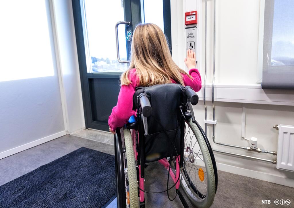 Ung jente i rullestol trykkjer på døropnarknapp. Foto.