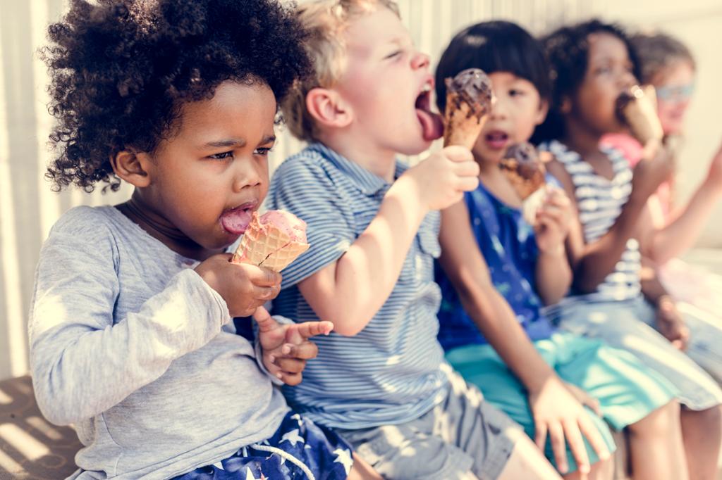 Fem barn sitter på rekke og tester iskrem. Foto.