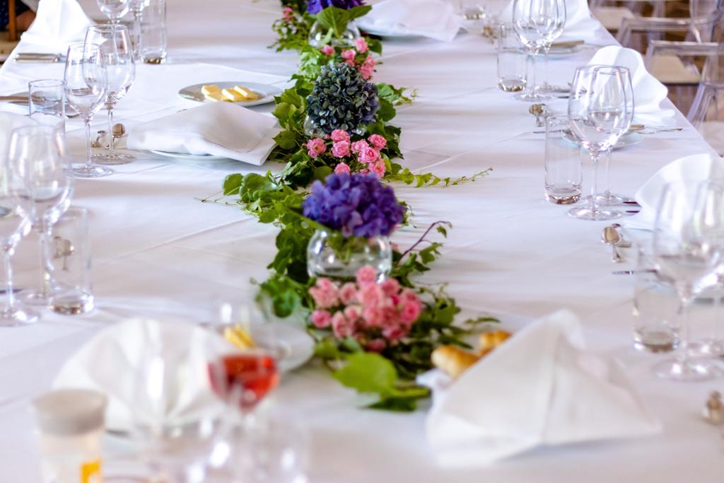 Et pent dekket bord med hvit duk og fargerike blomsteroppsatser. Foto.