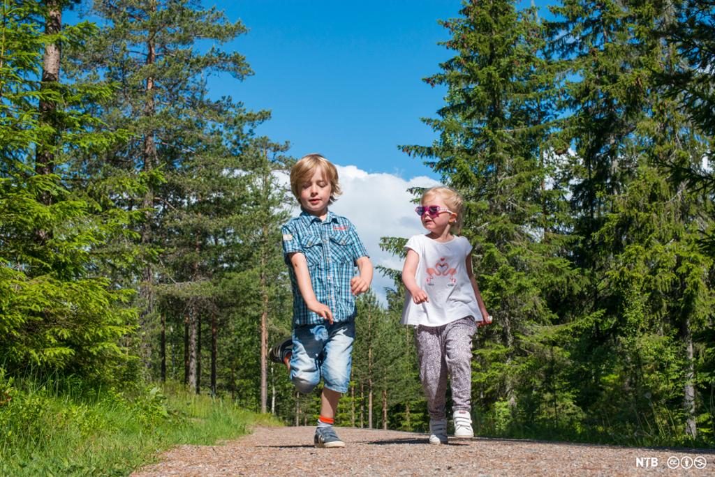 En gutt og ei jente som løper på en vei i skogen. Foto.