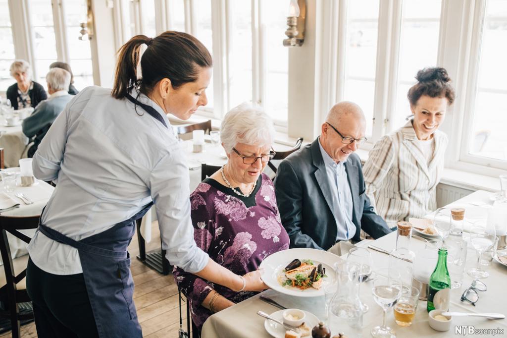En servitør setter en tallerken med mat foran en eldre dame. Foto.