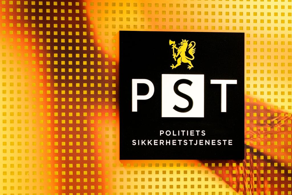 Politiets tryggingsteneste sin logo: PST og POLITIETS SIKKERHETSTJENESTE er skrive på svart bakgrunn. Ei gullfarga løve er trykt over skrifta. Foto.