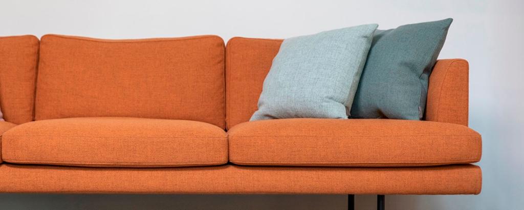 Oransje sofa med puter i kontrastfarger. Foto.