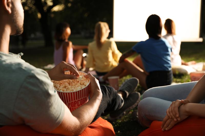 Ungdom med popcorn ser på film på en utendørs kino. Bilde.