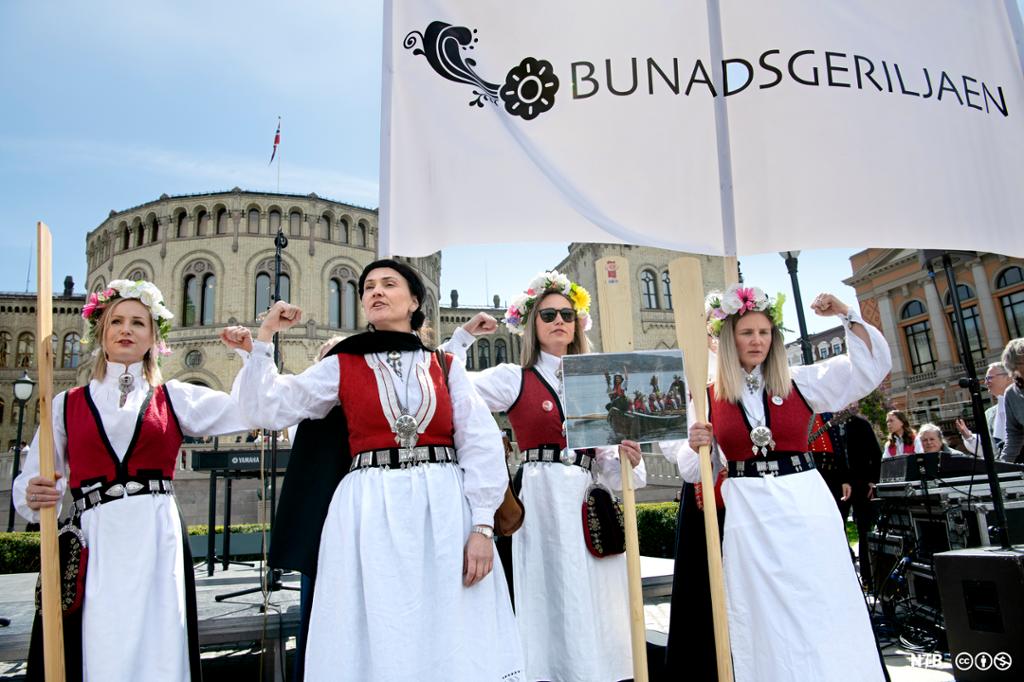 Fire bunadskledde kvinner med banner med teksten "Bunadsgeriljaen" flekser muskler foran Stortinget i Oslo. Foto.