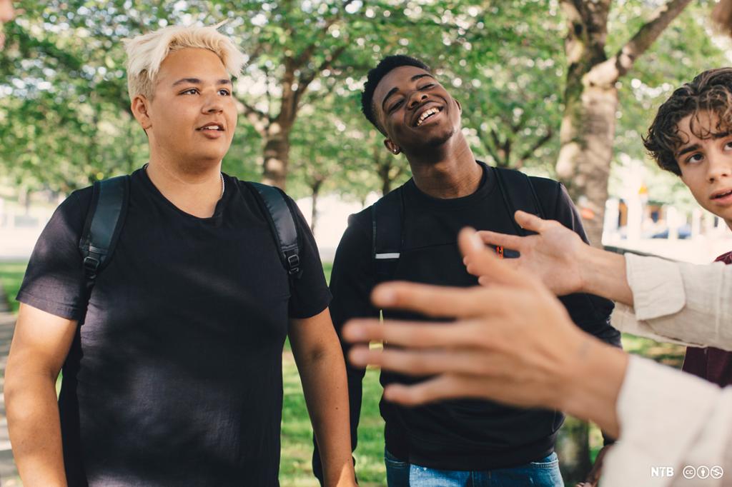 Unge gutar smiler og pratar saman i ein park. Foto.