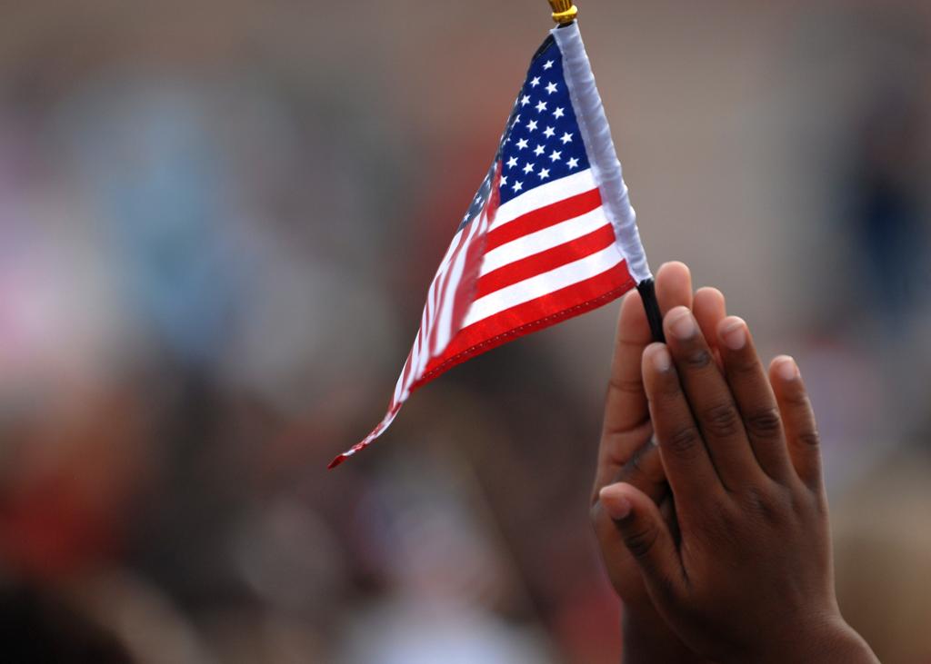 The hands of a Black child holding a small American flag. The palms of the hands are pressed together. Photo. 