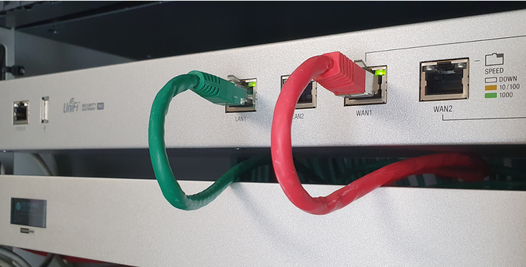 Rackmonter-ruter, en grønn nettverkskabel koblet til LAN1-port, en rød nettverkskabel koblet til WAN1-port. Foto.