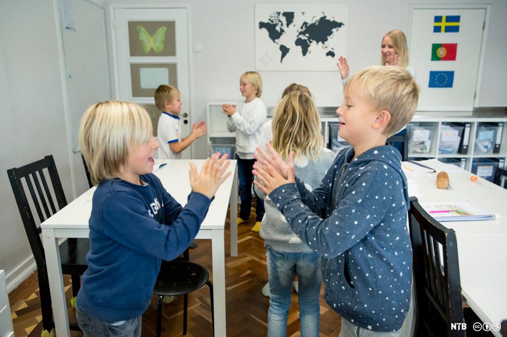 Barn leker klappelek inne i klasserommet. Foto.