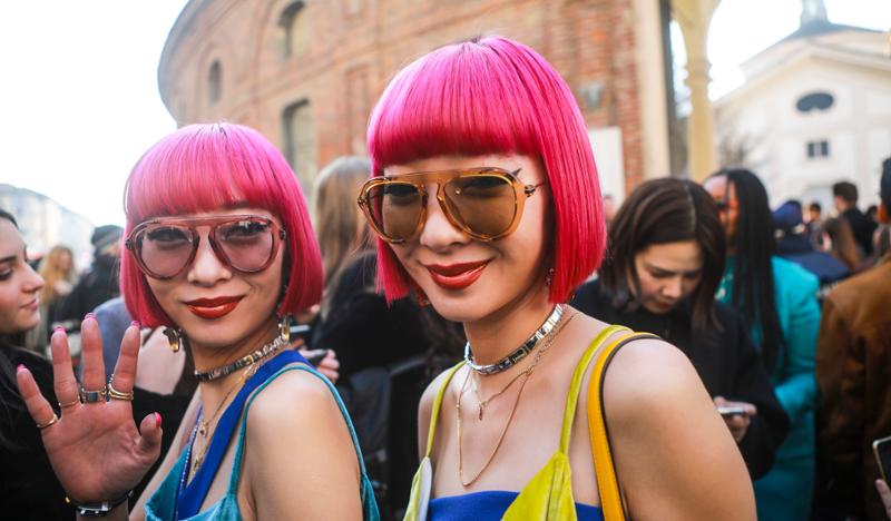 To unge kvinner som er tvillinger, med identisk rosa hår og like smykker og klær. Foto.