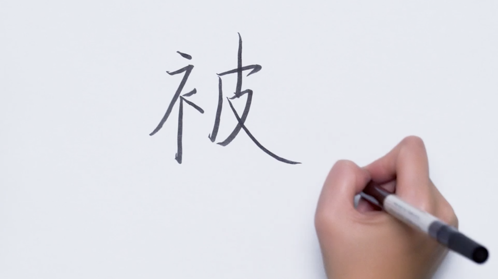 Hånd skriver et kinesisk skrifttegn med tusj. Foto.
