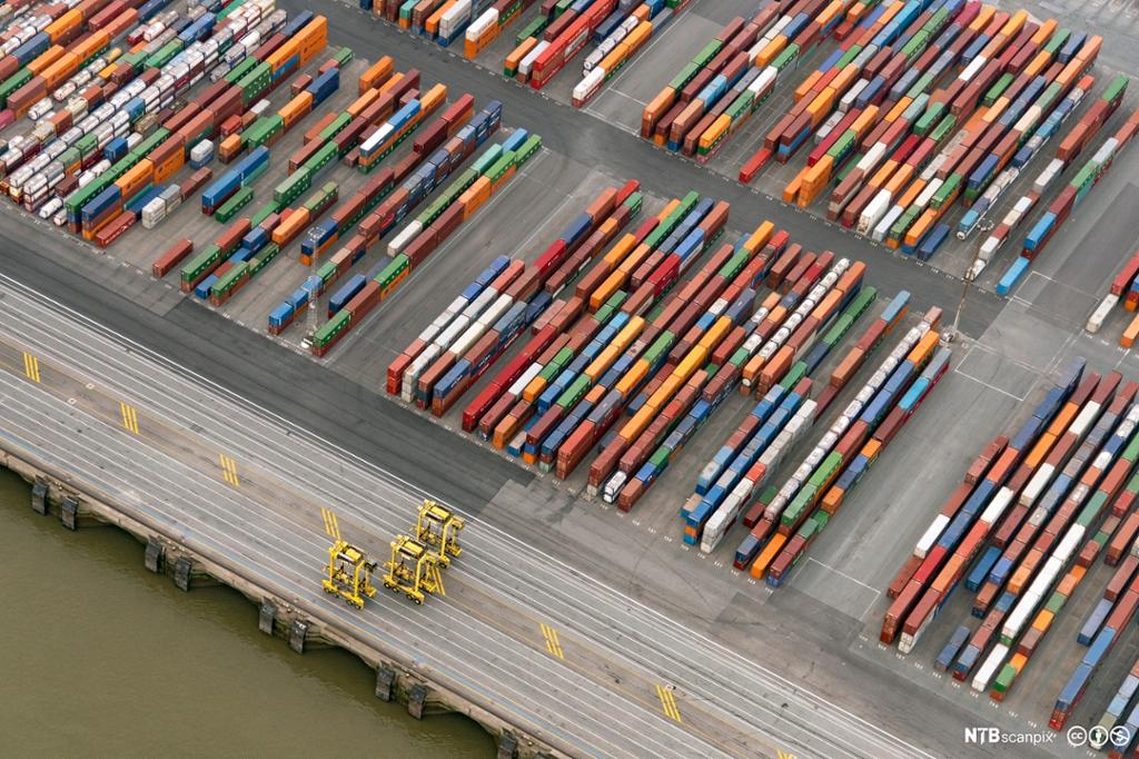 Mange konteinere i ulike farger på rekke og rad i et havneområde. Flyfoto. 