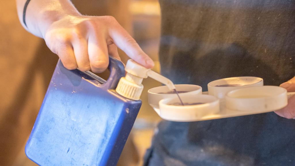 Ei hand holder en beholder med schalmvæske og bruker pekefingeren til å pumpe ut væska i et schalmbrett. Foto.