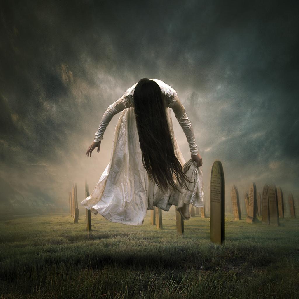 Photo art: A woman with long black hair, wearing a white dress, is floating above a graveyard. We cannot see her face. 