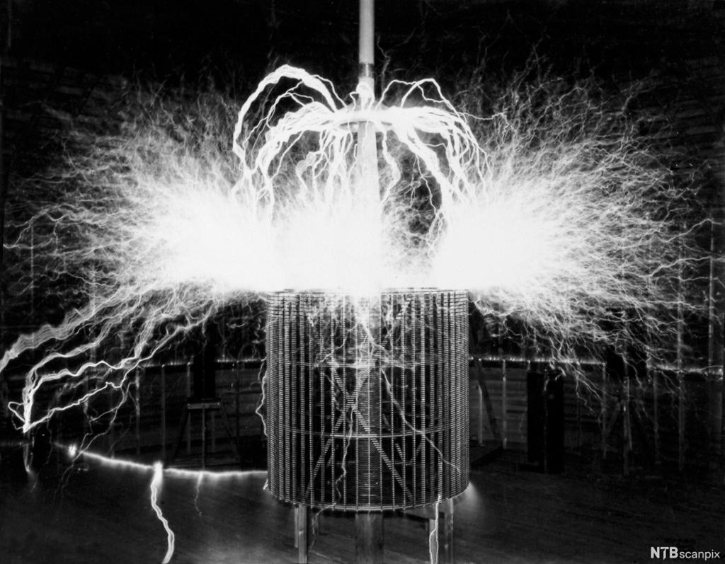 Black and white photo: We see a circular metal structure that is exposed to electric current, and we see a discharge of light coming from the structure. 