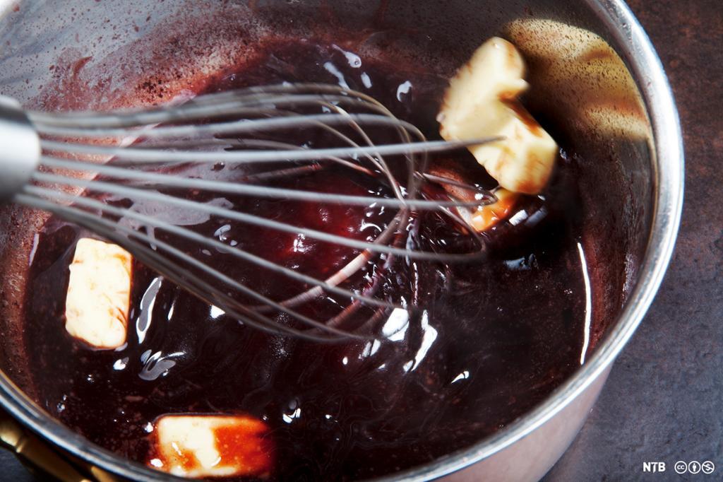 Smørklatter røres inn i en rødvinssaus. Foto.