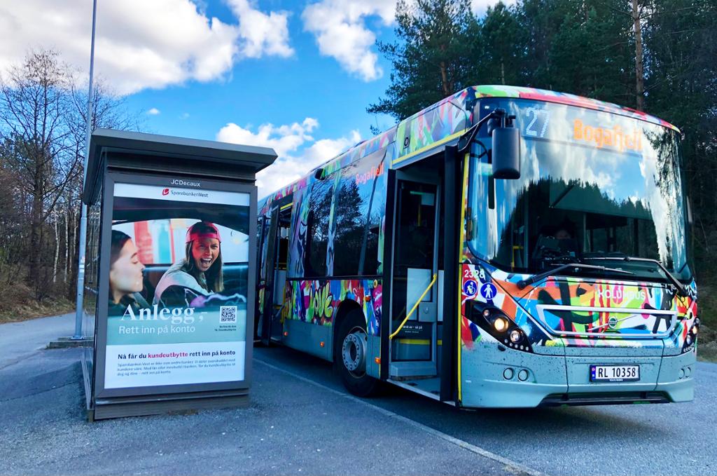 Busskur med reklame og ein dekorert buss. Foto.