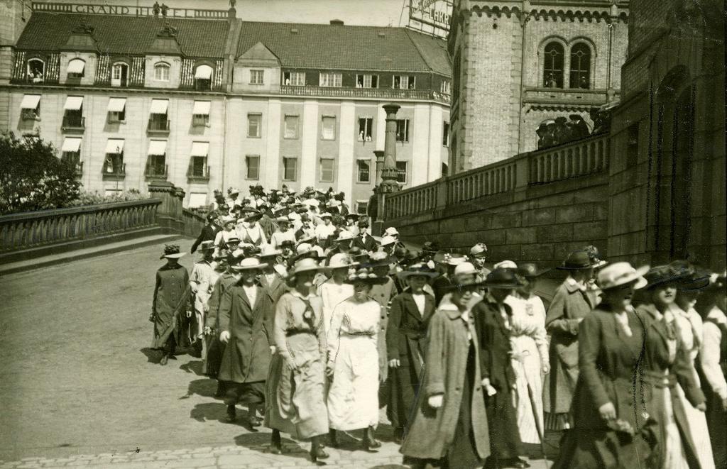 En stor folkeansamling foran Stortinget. De fleste på bildet er kvinner med kjoler, frakker og hatter. Foto. 