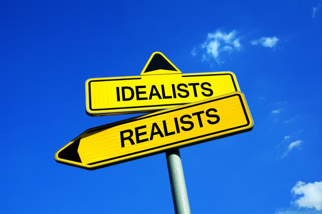 To veiskilt med påskrift "Realists" og "Idealists". Det første peker mot venstre, det andre opp mot himmelen. Foto.