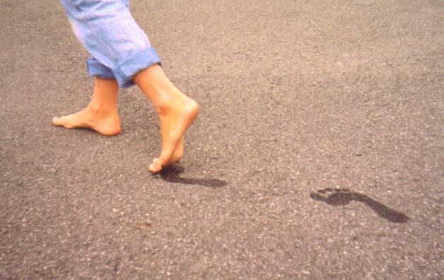 Barfotet person går bortover og etterlater seg fotspor på asfalten. Foto.