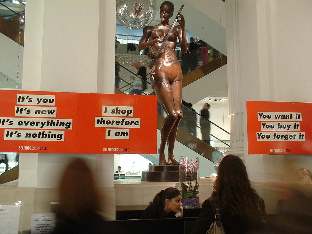 En butikk med ei rekke salgsplakater der det blant annet står "I shop therefore I am". Foto. 