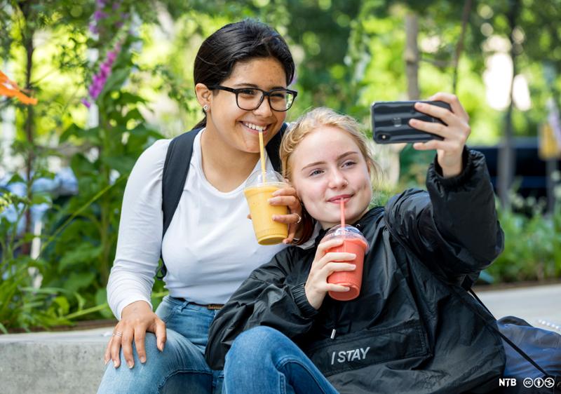 To jenter som drikker smoothie og tar selfie. Foto.  