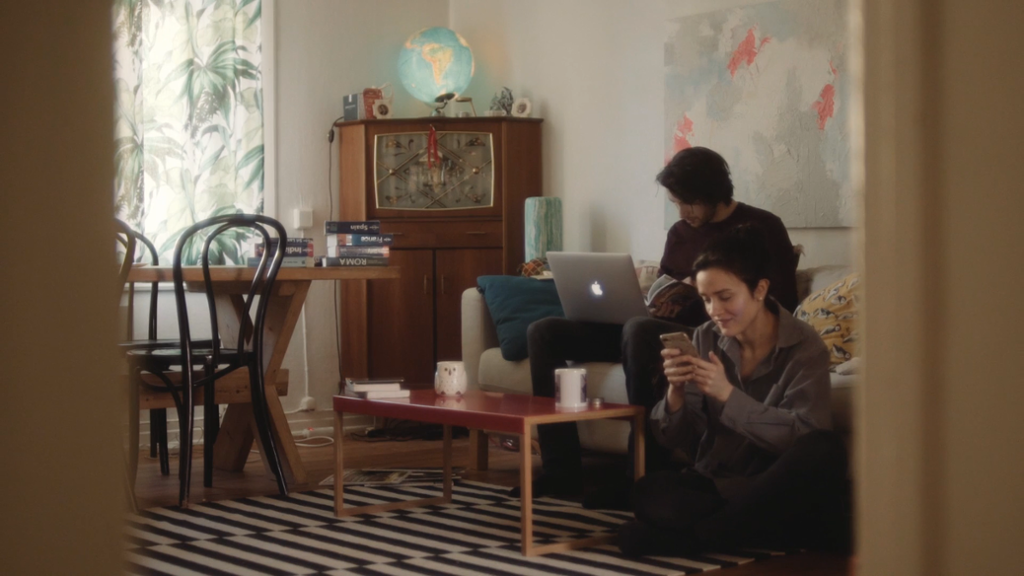 Gutt og jente sitter i ei stue med pc og mobil. Foto.