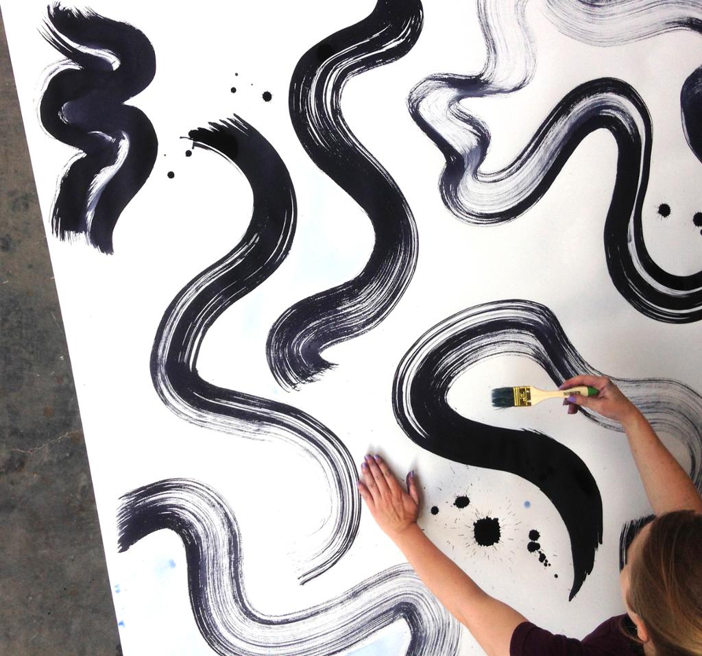 Designer maler buede streker i sort på stort format. Foto.